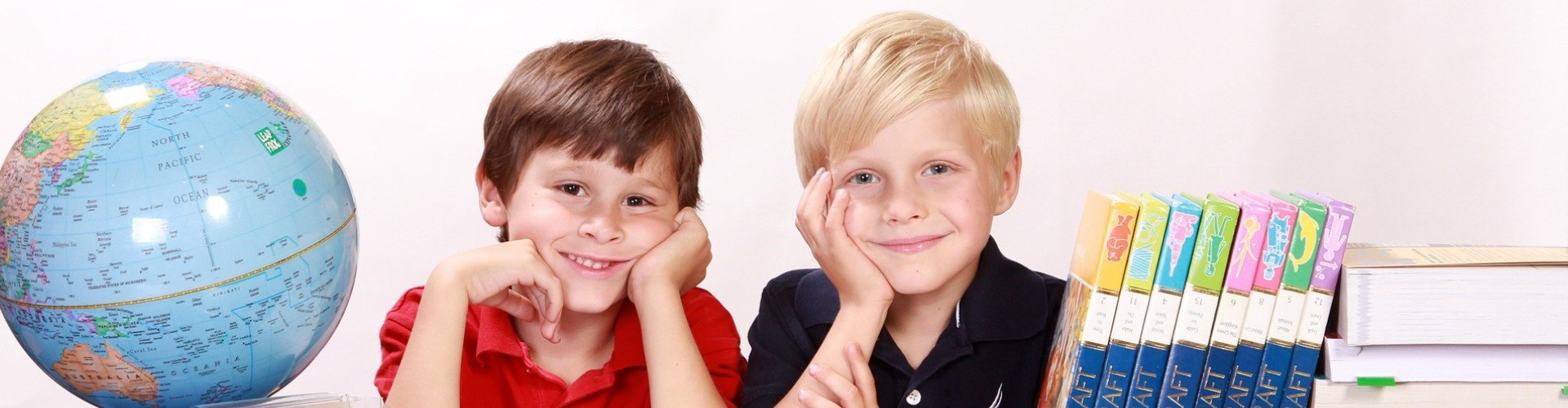 Two boys study between books and a globe at Creative Paths Learning Studio.